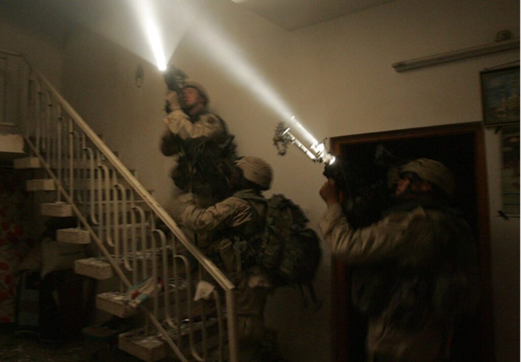 David Bellavia and two other soldiers with guns and lights going up a staircase